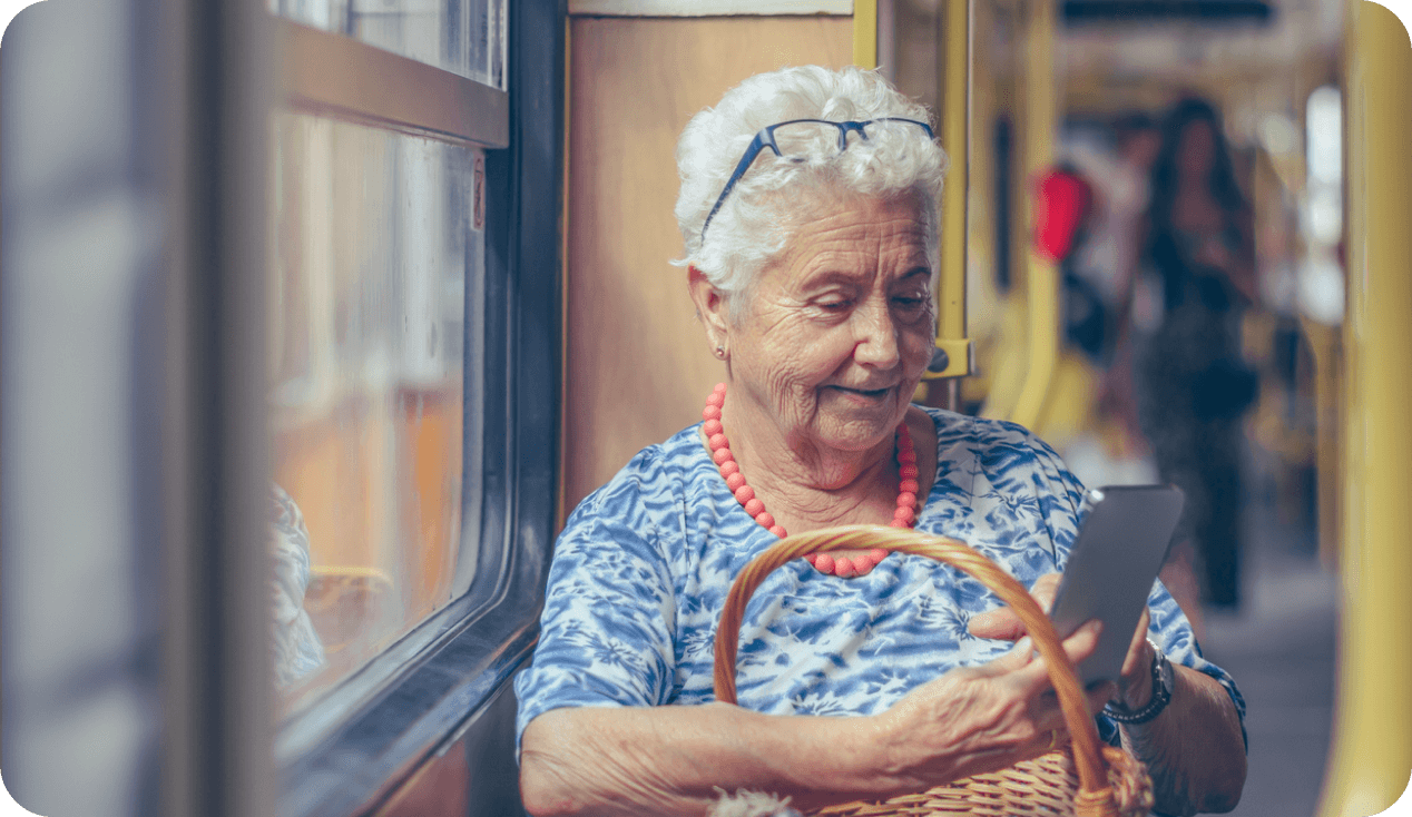 Una mujer adulta mayor revisa su app bancaria desde el celular mientras viaja en transporte público.