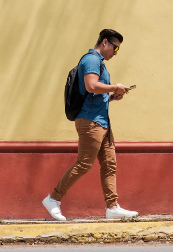 Un joven caminando por la calle mientras revisa su celular.