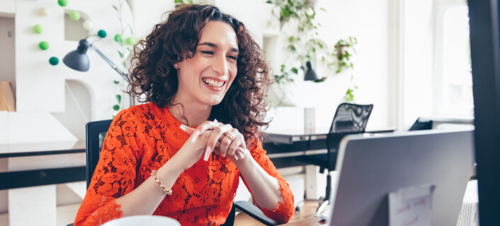 Una mujer sentada en su escritorio sonriendo frente a su laptop.