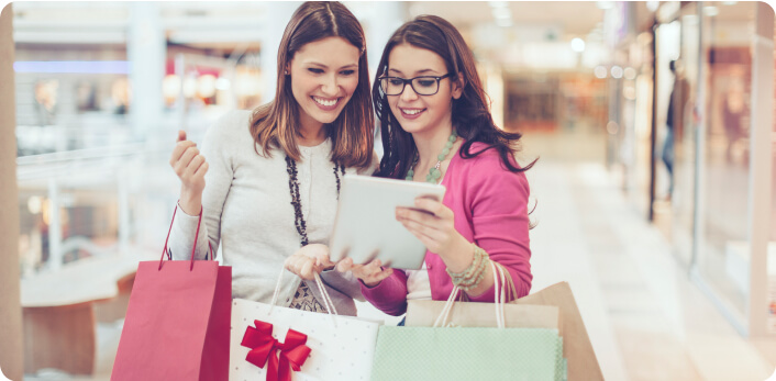 Dos mujeres sosteniendo sus bolsas de compras mientras revisan una tablet.