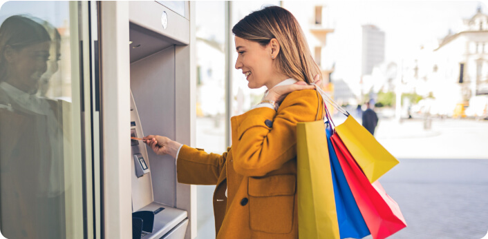Una mujer sosteniendo sus compras mientras saca dinero de un cajero automático.