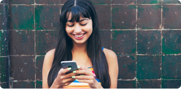 Una mujer sonriendo mientras utiliza su celular.