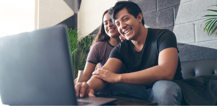 Una pareja sentada en un sofá mientras utiliza una laptop.