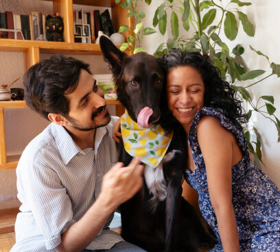Una pareja sonriendo mientras están abrazando a un perro.