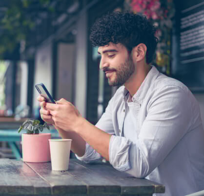 Un hombre sentado mientras utiliza su celular.