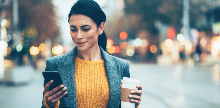 Mujer sostiene un café mientras revisa su app Banamex en el celular.