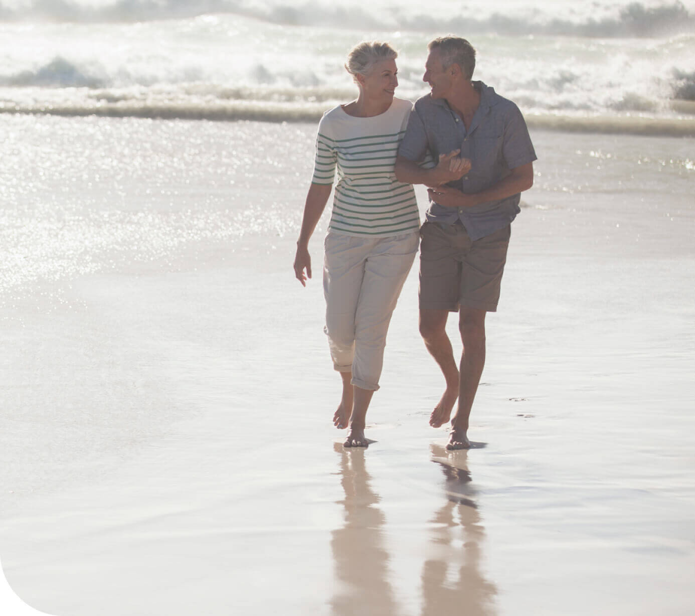 Pareja sonriente camina por la playa al atardecer.