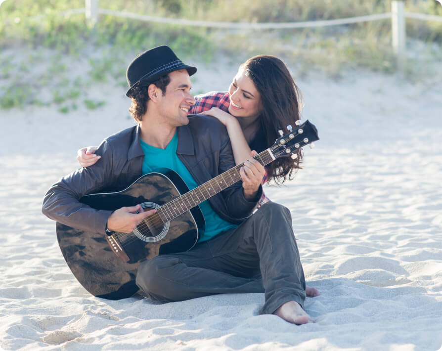 Hombre toca la guitarra en la playa mientras su pareja lo abraza.