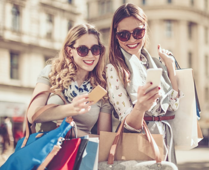 Dos mujeres sonriendo con bolsas de compras y sosteniendo una tarjeta de crédito en la mano.