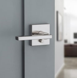 Manija de palanca moderna con llave y placa cuadrada en acero para puerta de entrada.