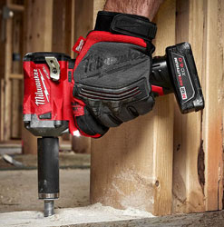 Mano con guante usando llave de impacto Milwaukee roja atornillando una viga de madera